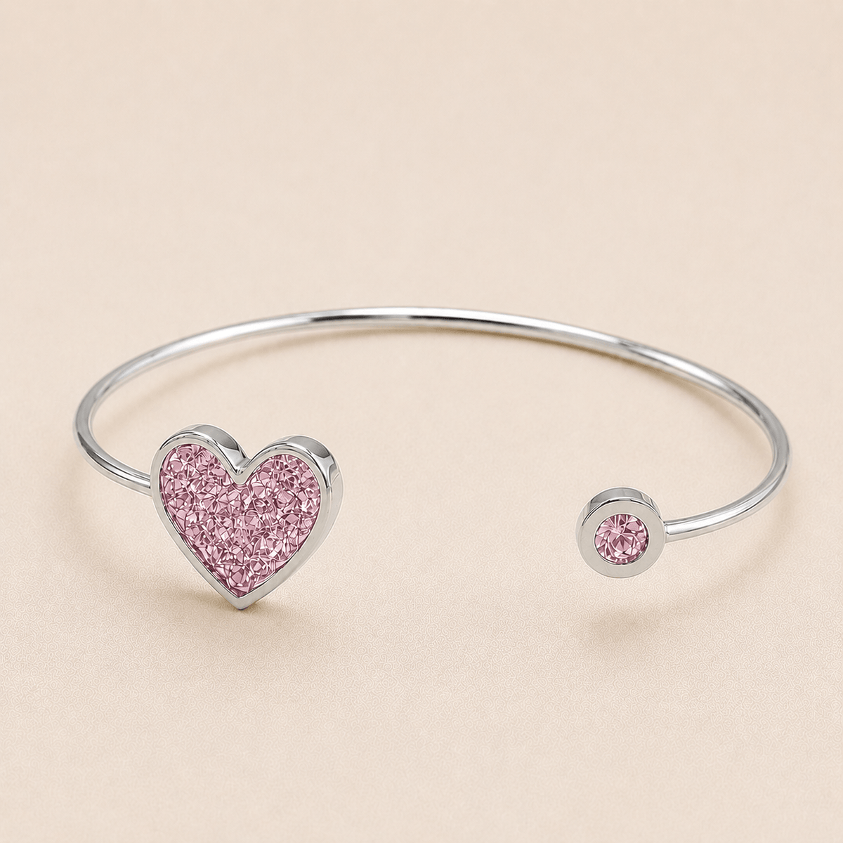 silver-tone open cuff bangle bracelet featuring a glittery pink heart charm on one end and a smaller matching pink heart
