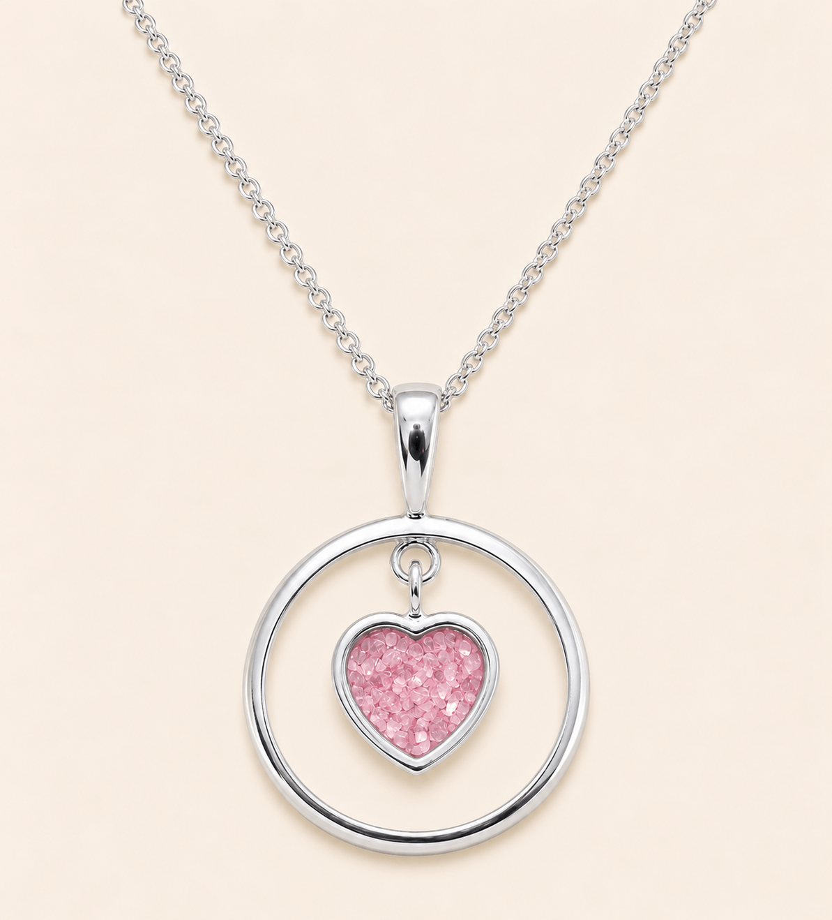 A silver necklace featuring a circular open pendant with a dangling glittery pink heart charm, displayed on a light beige background.
