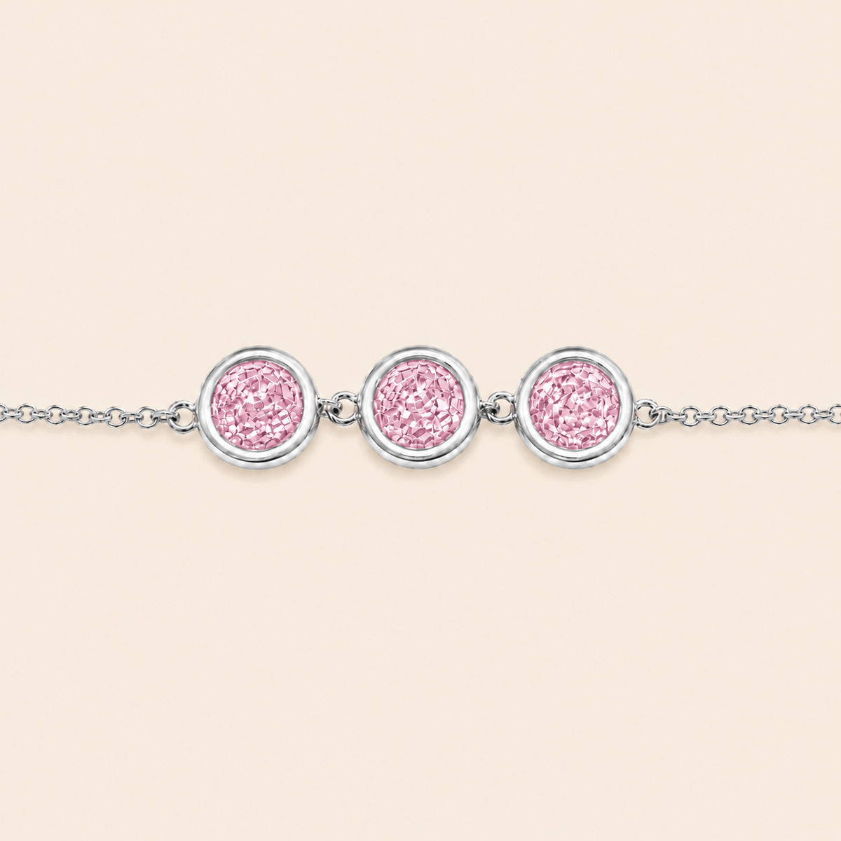 A silver chain bracelet featuring three circular bezel-set pink textured stones, displayed against a solid pale beige background.